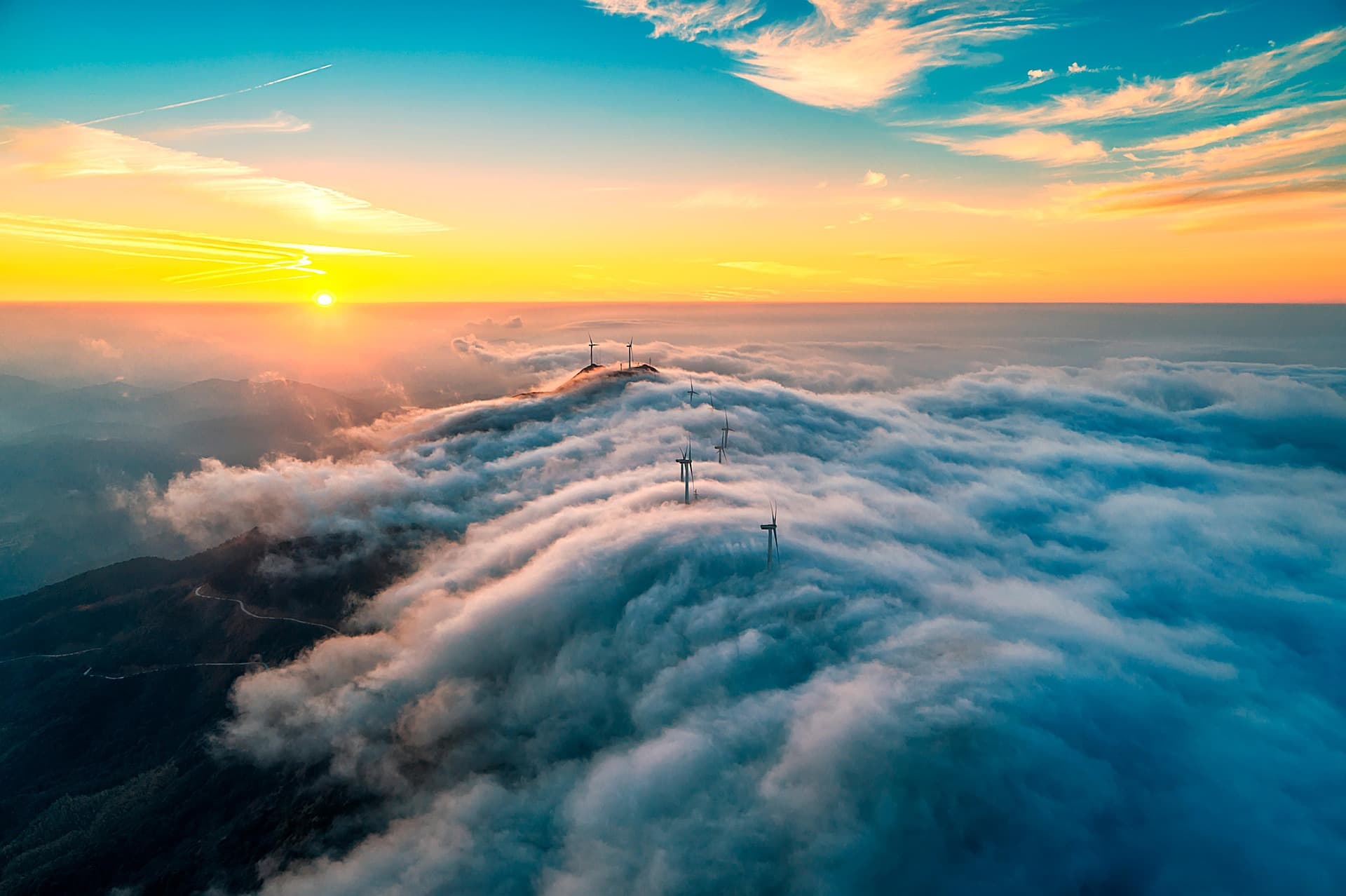Wind turbines emerging from clouds at sunset